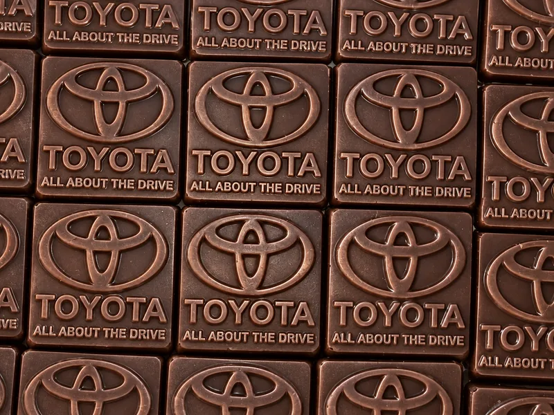 Rows of square chocolate plaques, each moulded with a car maker’s logo and tagline pressed into the surface, painted bronze
