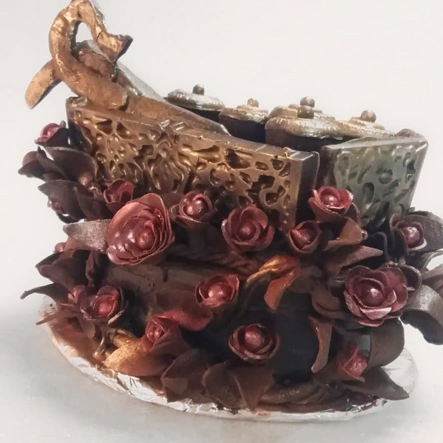 Coklat tepak sireh buatan tangan, berdinding tebuk bersalut emas dan perak, dengan cembul bertutup di atasnya, hiasan coklat melengkung, serta bunga ros dan daun coklat merah marun di sekelilingnya